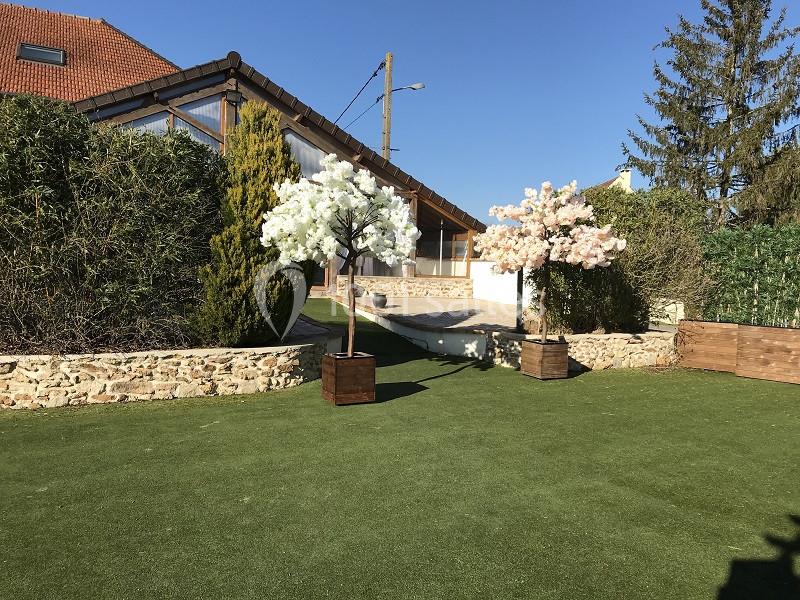 Deux arbres artificiels fleuris, blanc et rose, décorent un jardin avec pelouse synthétique et muret en pierre.