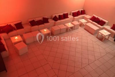 Salle de réception décorée avec des guirlandes lumineuses, des lanternes suspendues et des tables dressées pour un événement.