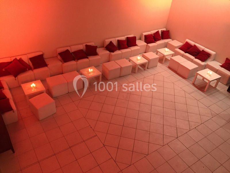 Salle avec des canapés blancs, coussins rouges et petites tables éclairées par des bougies, ambiance tamisée.