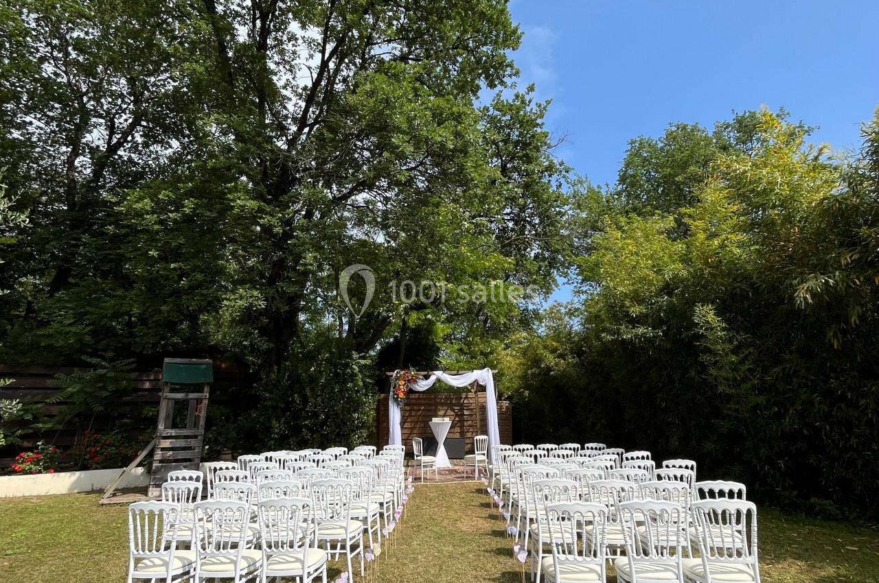 Chaises blanches disposées en rangées sur une pelouse, face à une arche décorée pour une cérémonie en extérieur.