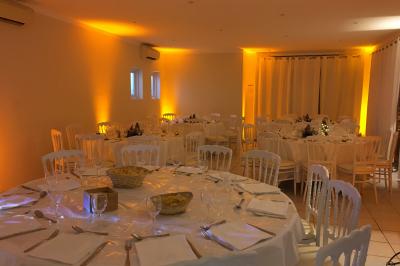 Salle de réception décorée avec des guirlandes lumineuses, des lanternes suspendues et des tables dressées pour un événement.