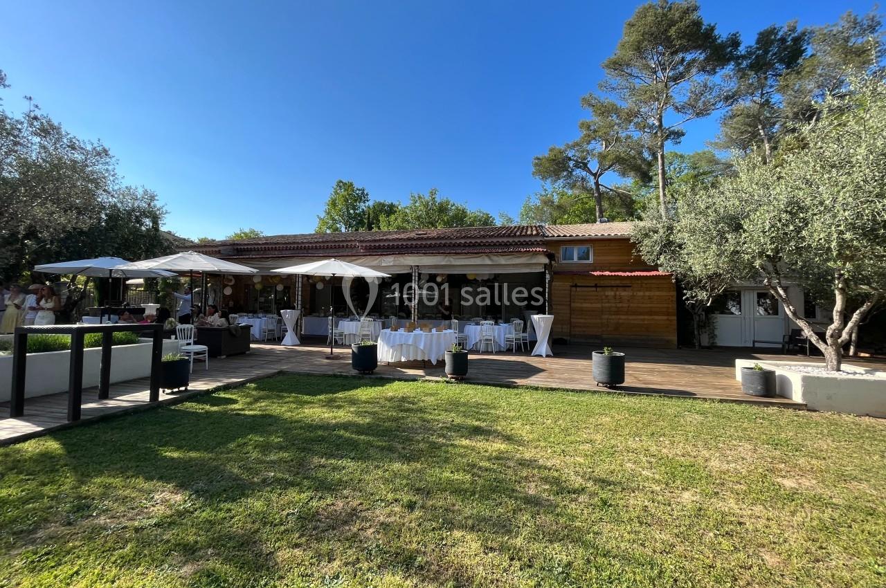Terrasse aménagée avec tables dressées sous des parasols, entourée de verdure et d'arbres par une journée ensoleillée.