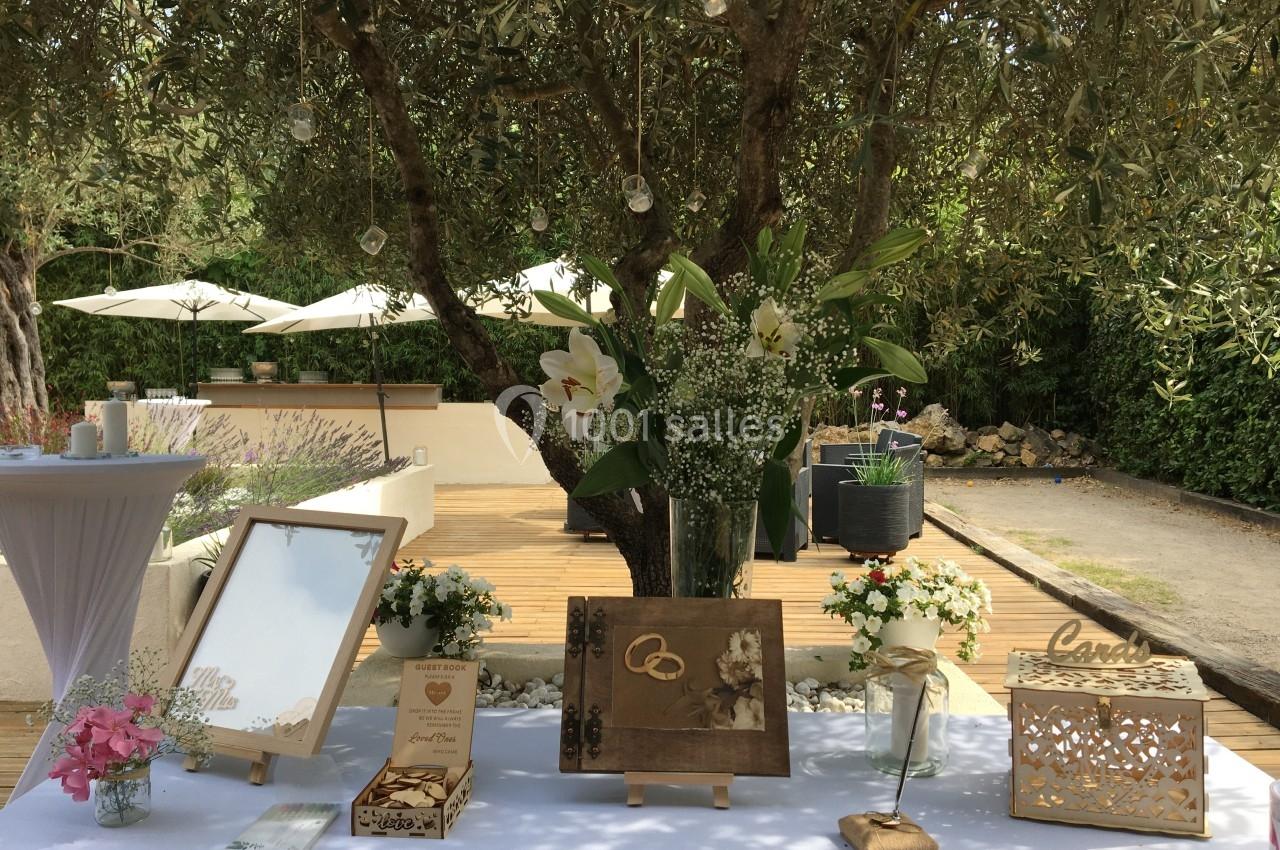 Table décorée pour un mariage en extérieur, avec fleurs, cadres, livre d'or et ornements sous un olivier.