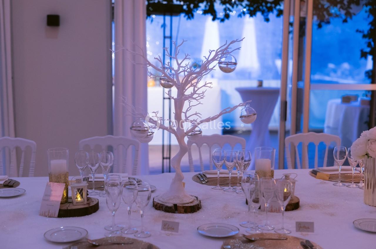 Table décorée pour un événement avec un arbre blanc central orné de boules transparentes et des verres disposés autour.
