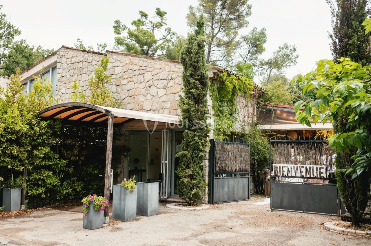 Façade d'un bâtiment en pierre entouré de végétation, avec une entrée couverte et un panneau ’Bienvenue’.