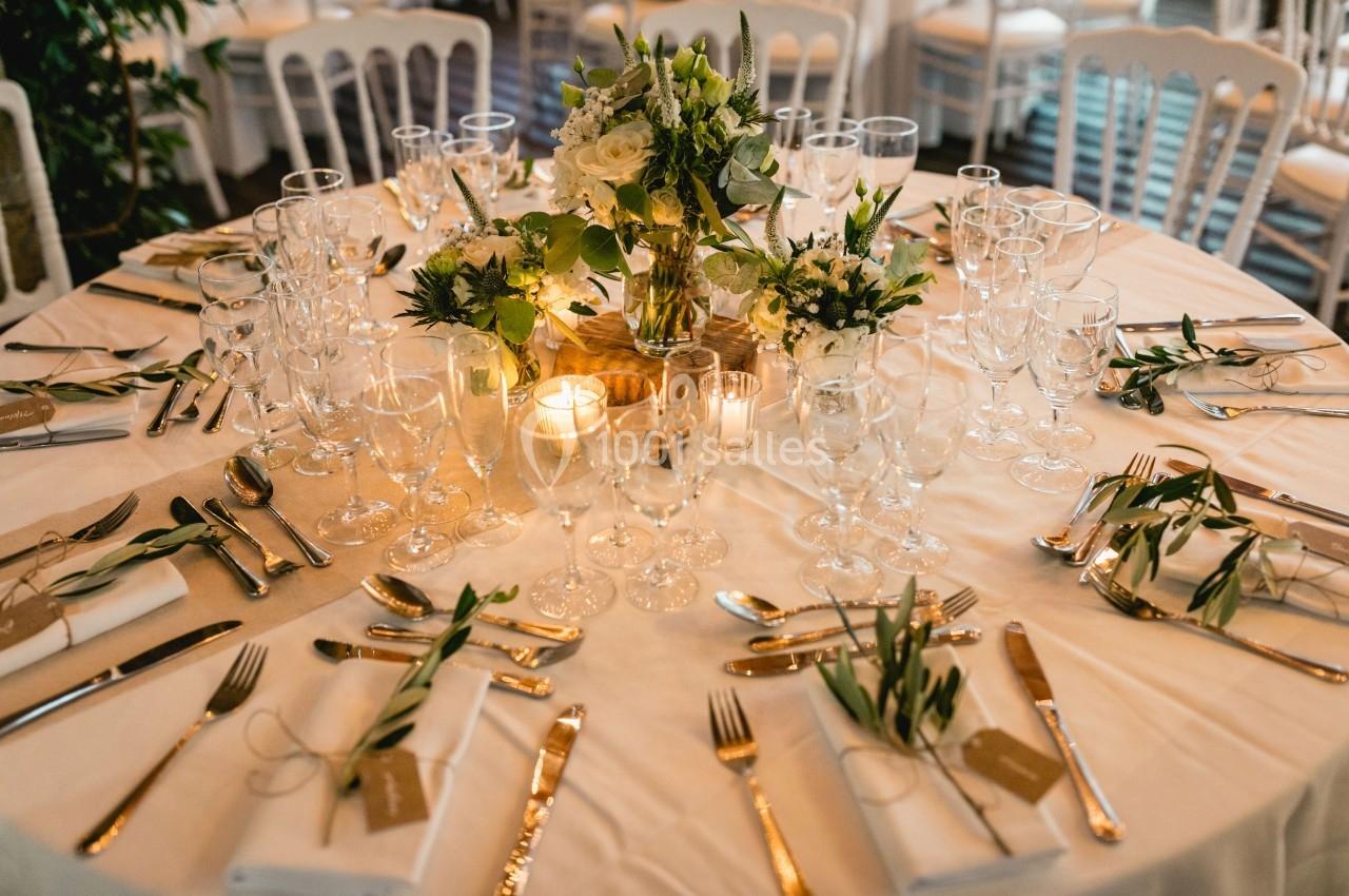 Table élégamment dressée avec des couverts dorés, verres en cristal, bougies et compositions florales au centre.