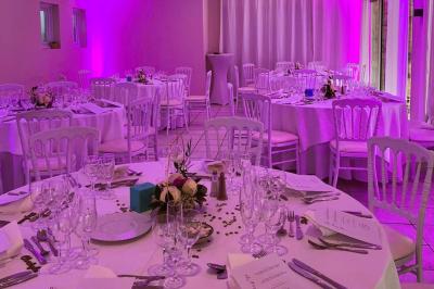 Salle de réception décorée avec des guirlandes lumineuses, des lanternes suspendues et des tables dressées pour un événement.