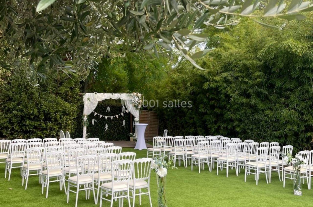 Chaises blanches disposées en rangées sur une pelouse, face à une arche décorée pour une cérémonie en extérieur.