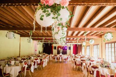 Salle de réception lumineuse avec des tables rondes dressées, nappes blanches et chaises rouges.