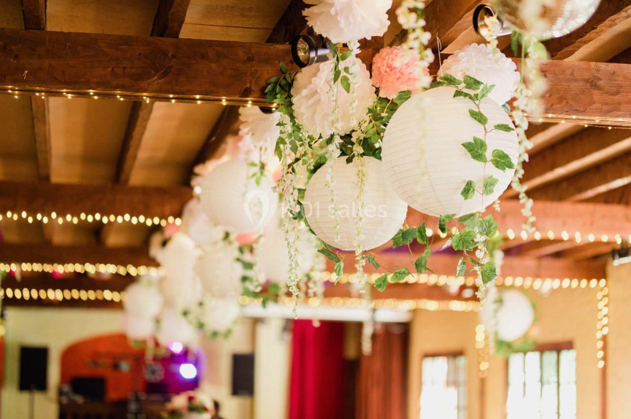 Guirlandes lumineuses et lanternes blanches décorées de feuillage suspendues sous un plafond en bois.