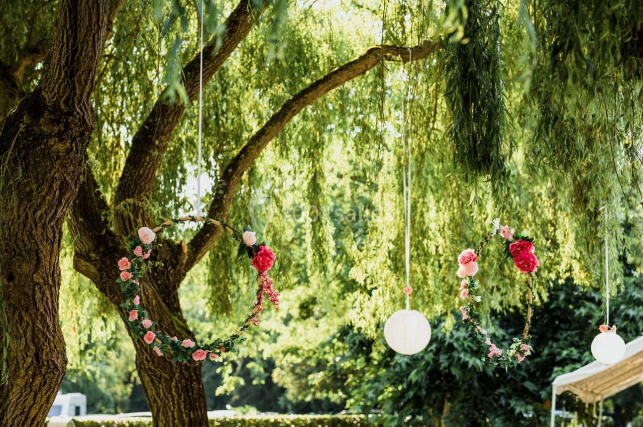 Anneaux décoratifs ornés de fleurs suspendus à des branches d'arbre sous un feuillage dense et lumineux.