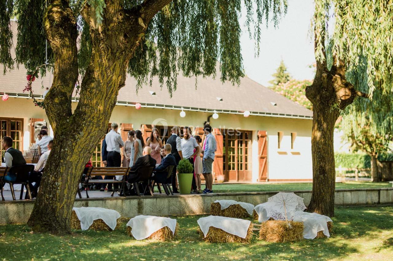 Groupe de personnes discutant près d'un bâtiment, avec des bottes de paille décorées au premier plan sous des arbres.