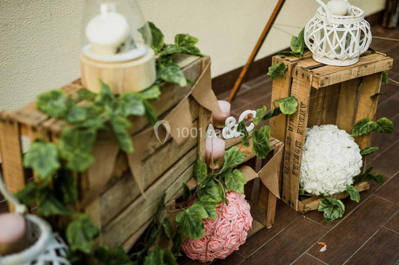 Décoration en bois avec feuillage, lanternes blanches et boules de fleurs roses et blanches sur un sol en bois.