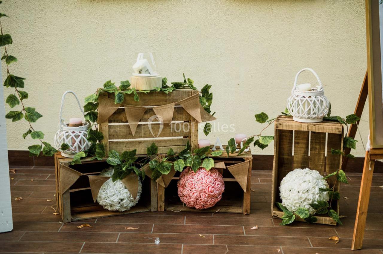 Décoration rustique avec caisses en bois, guirlandes de feuillage, lanternes blanches et boules de fleurs.