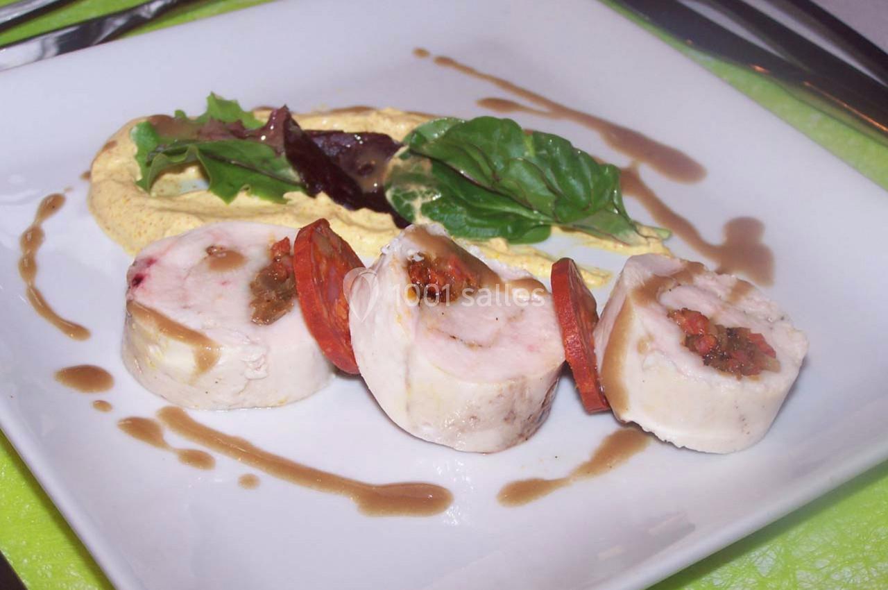 Roulés de volaille garnis, accompagnés de légumes, sauce et purée disposés sur une assiette blanche.