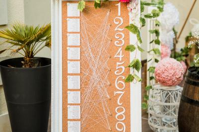 Salle de réception lumineuse avec des tables rondes dressées, nappes blanches et chaises rouges.
