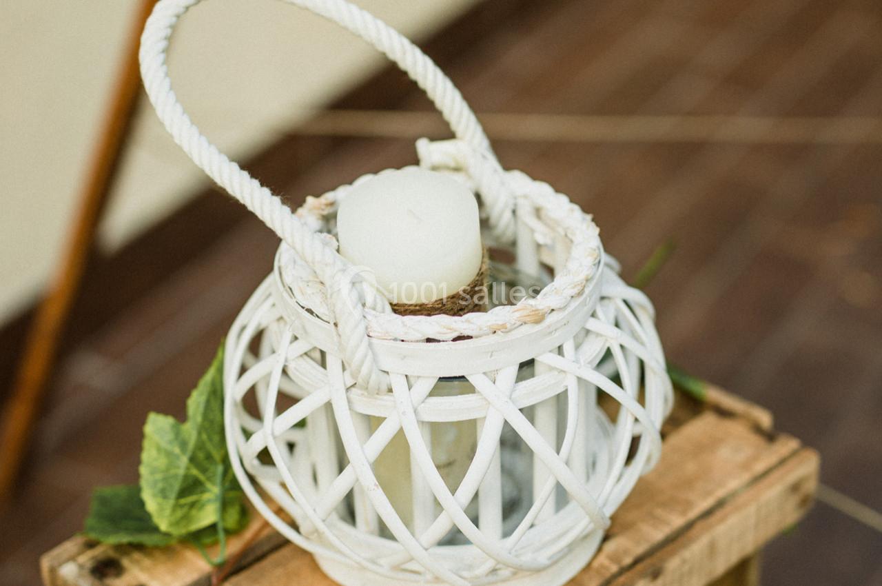 Lanterne blanche en osier avec une bougie à l'intérieur, posée sur une caisse en bois avec des feuilles décoratives.