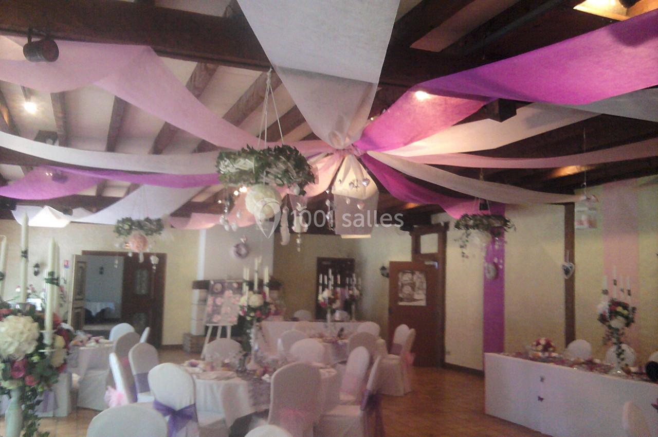 Salle de réception décorée avec des rubans colorés suspendus au plafond et des tables dressées pour un événement.