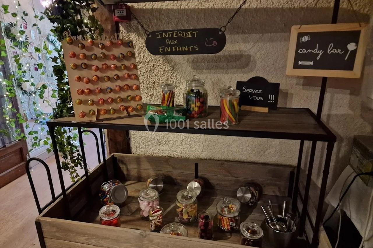 Présentoir en bois avec bonbons variés en bocaux et panneau ’Interdit aux enfants’ sur un mur clair.