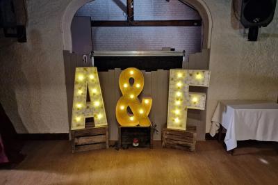 Salle de réception lumineuse avec des tables rondes dressées, nappes blanches et chaises rouges.