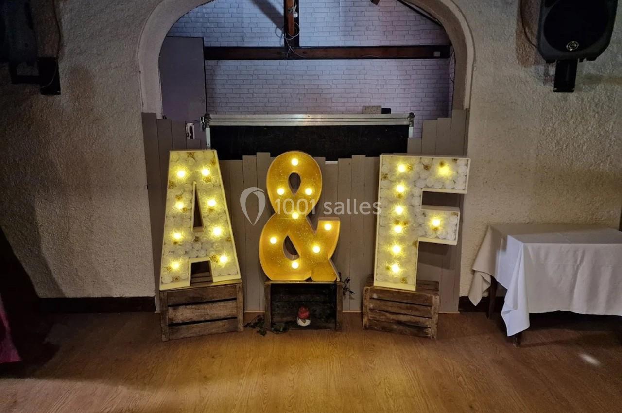 Lettres lumineuses ’A’ et ’F’ avec une esperluette, posées sur des caisses en bois devant un mur clair.