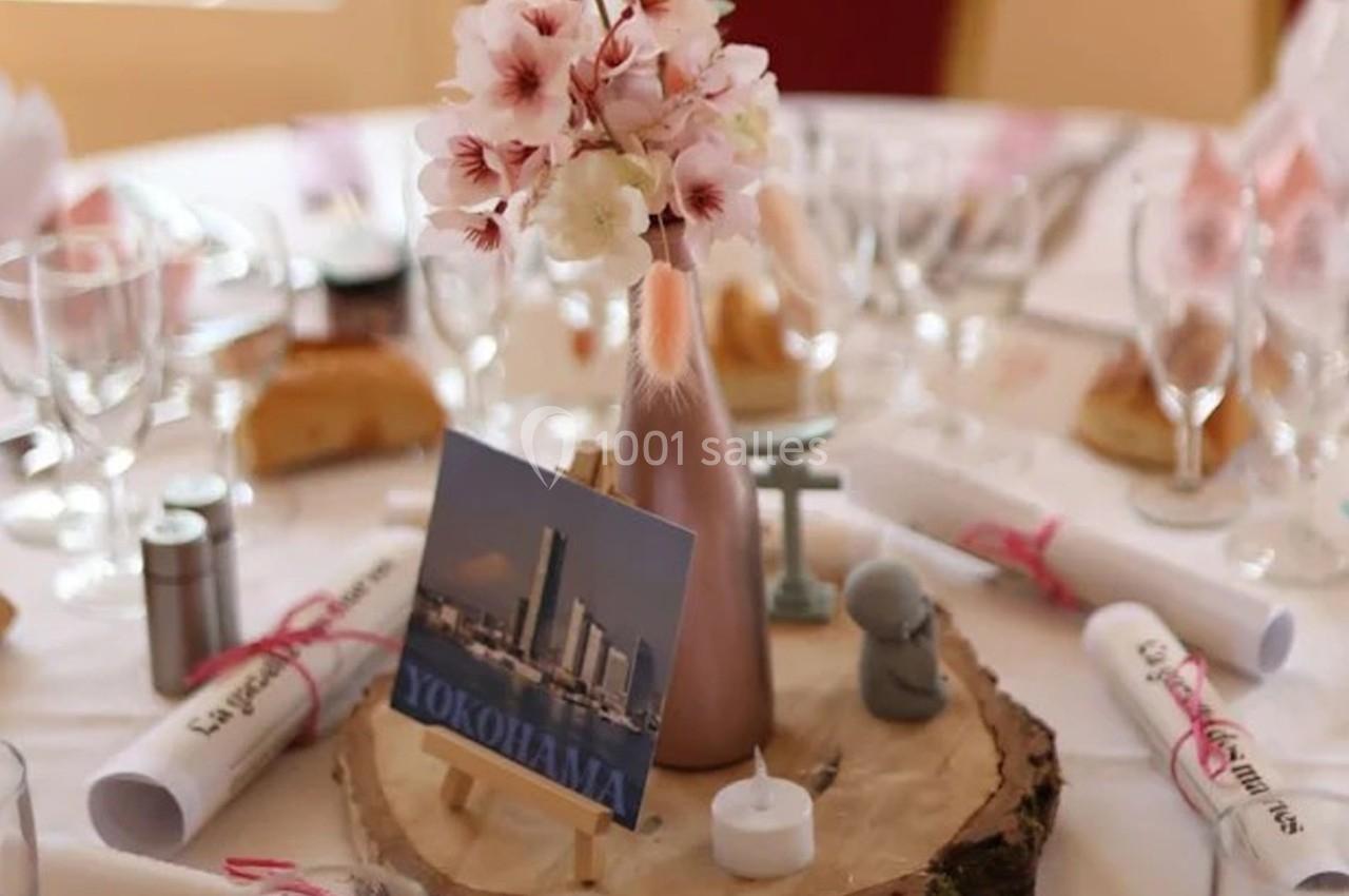 Centre de table avec vase rose, fleurs, carte ’Yokohama’, bougie et rondin de bois, entouré de verres et serviettes.