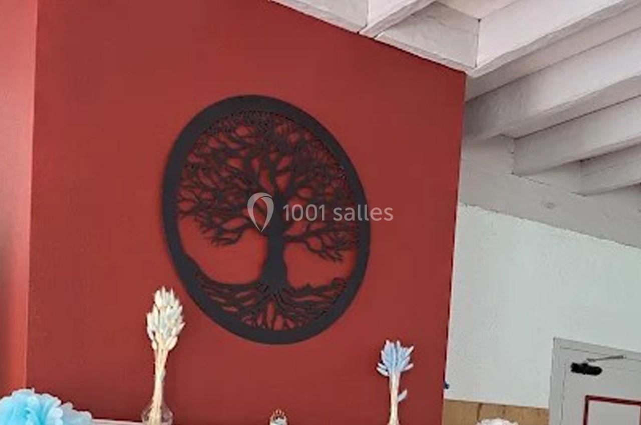 Décoration murale représentant un arbre stylisé en métal noir sur un mur rouge, entourée de petites sculptures.