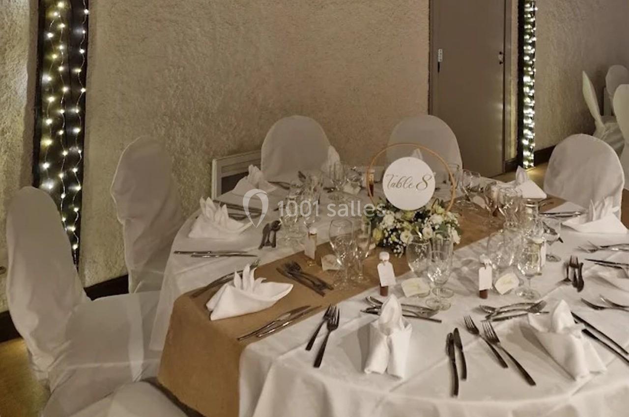 Table ronde décorée pour un événement, avec nappes blanches, centre de table floral et couverts disposés.