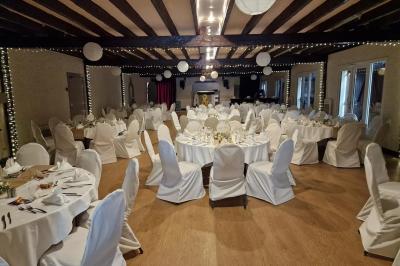 Salle de réception lumineuse avec des tables rondes dressées, nappes blanches et chaises rouges.