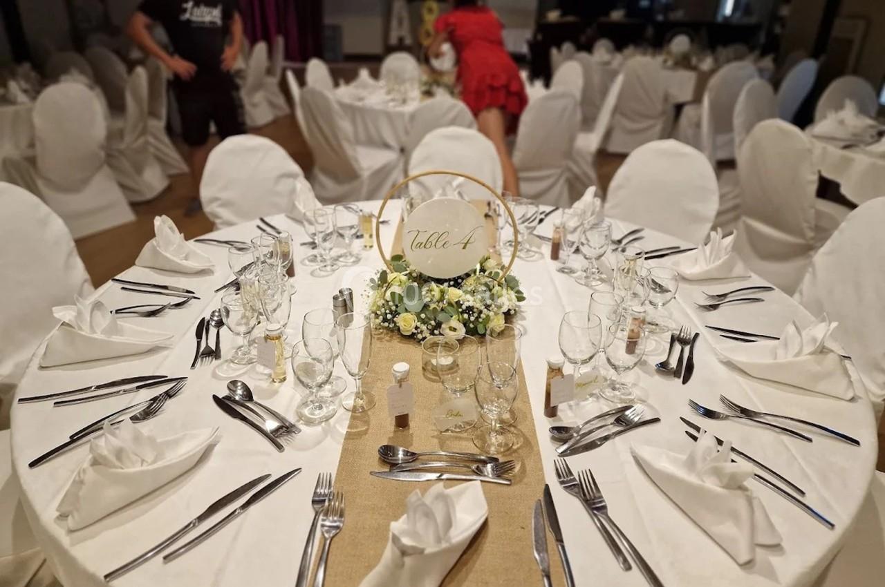 Table dressée pour un événement, avec nappes blanches, couverts disposés, centre de table floral et panneau ’Table A’.