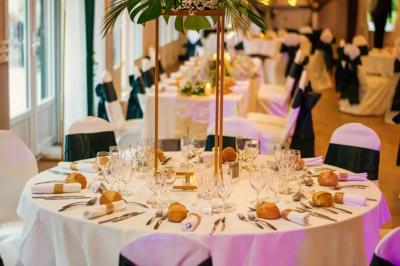Salle de réception lumineuse avec des tables rondes dressées, nappes blanches et chaises rouges.