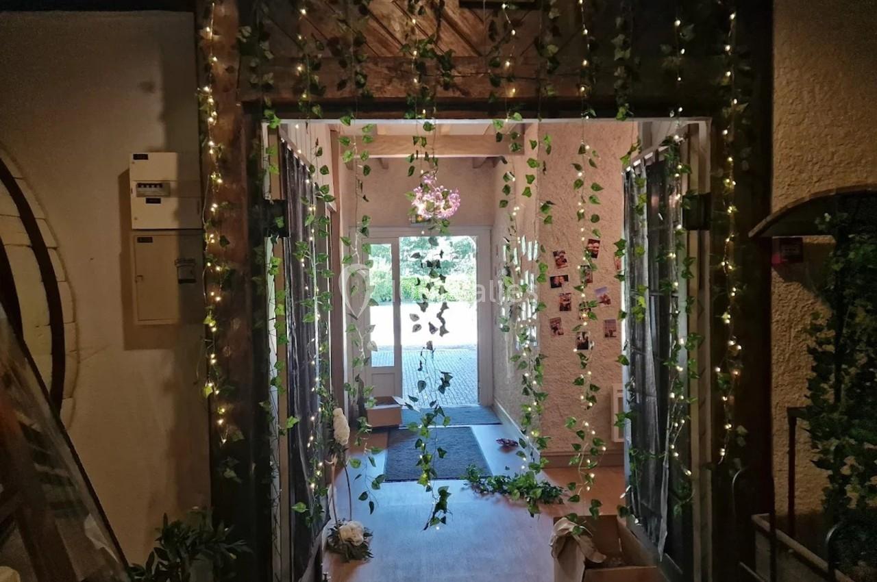 Entrée décorée de guirlandes lumineuses et de feuillages, avec une porte vitrée donnant sur l'extérieur en arrière-plan.