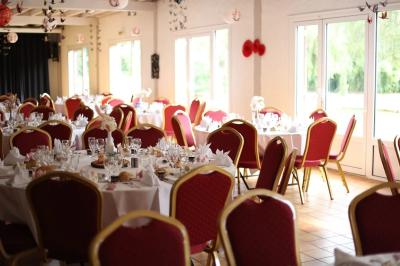 Salle de réception lumineuse avec des tables rondes dressées, nappes blanches et chaises rouges.