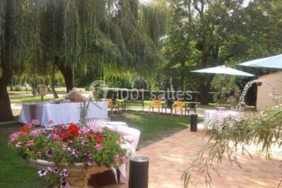 Salle de réception lumineuse avec des tables rondes dressées, nappes blanches et chaises rouges.