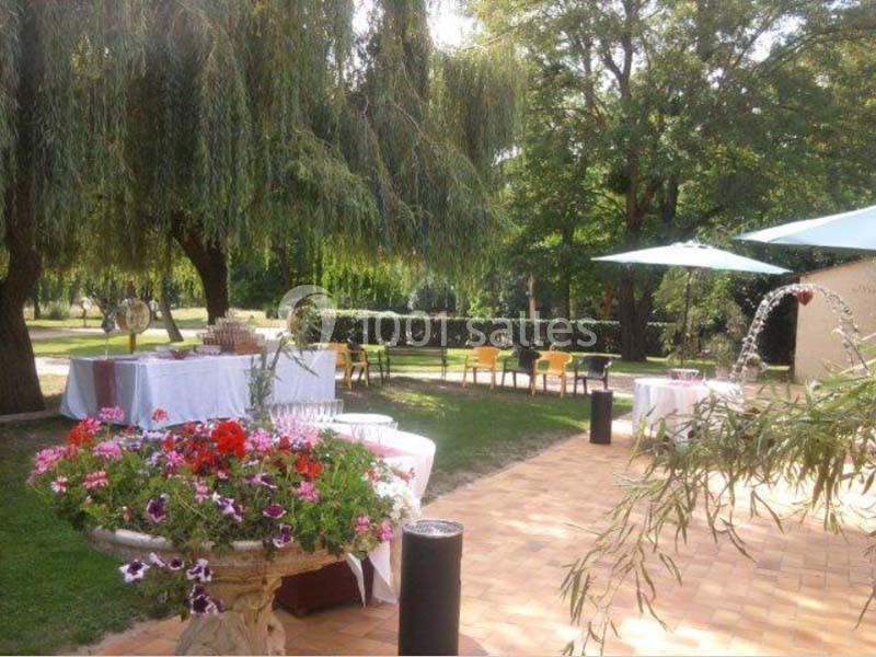 Terrasse ensoleillée avec tables dressées, chaises colorées, parasols et végétation luxuriante en arrière-plan.