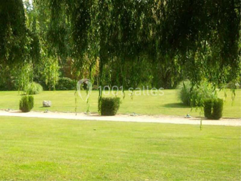 Pelouse verdoyante bordée d'arbustes et surplombée de branches tombantes de saules pleureurs.