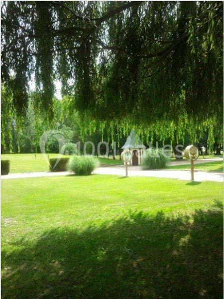 Un jardin verdoyant avec un petit bâtiment en arrière-plan, entouré d'arbres et de pelouses bien entretenues.