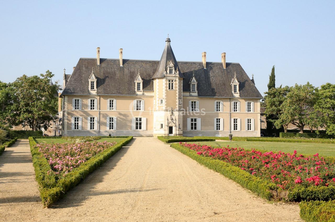 Façade d'un château historique entouré de jardins fleuris et d'une allée centrale en gravier.