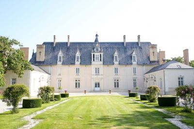 Façade d'un château avec une tour centrale et des fenêtres, entouré de végétation.