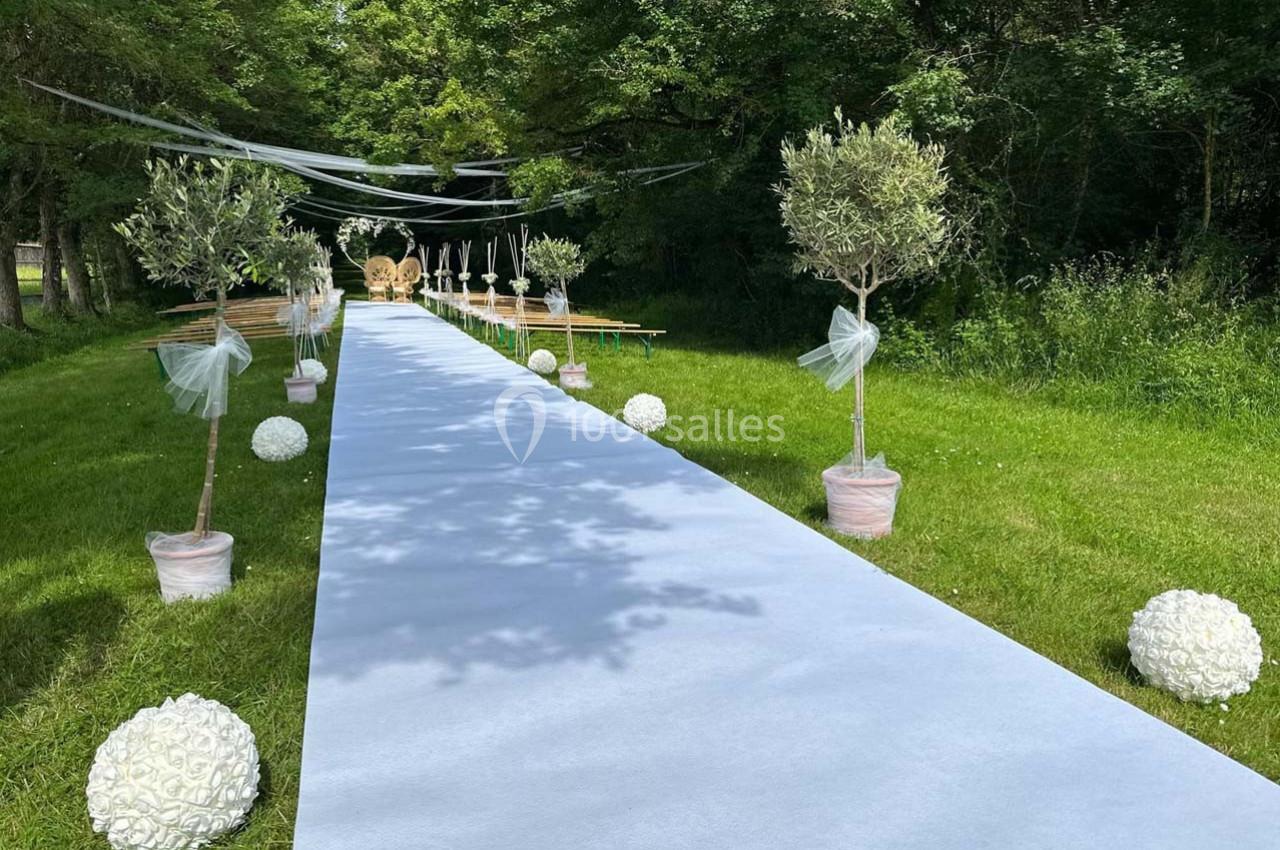 Allée extérieure décorée pour un événement, bordée d'arbres en pot et de boules blanches, menant à des sièges.