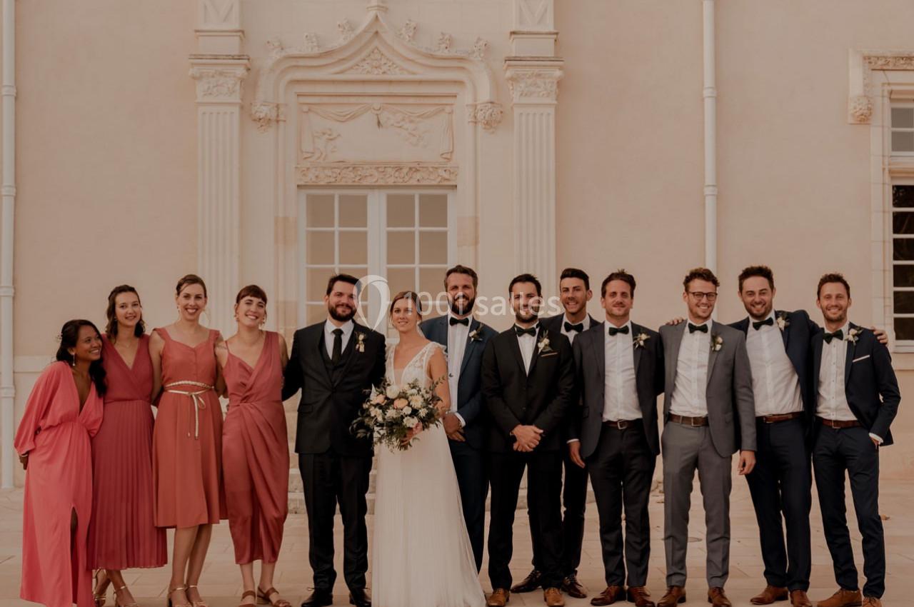 Un groupe de personnes posant devant un bâtiment clair avec une mariée en robe blanche au centre.