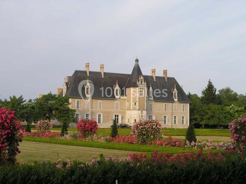 Manoir entouré de jardins fleuris avec des rosiers et une pelouse bien entretenue, sous un ciel clair.