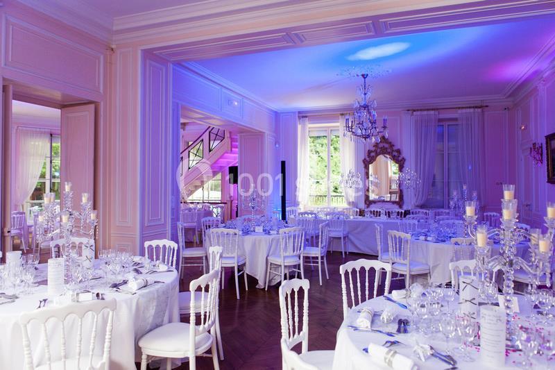Salle de réception élégante avec tables dressées, chaises blanches et éclairage tamisé dans un décor raffiné.