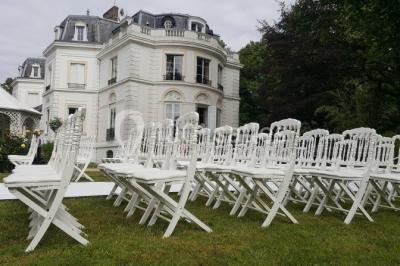 Allée bordée d'arbustes menant à une grande maison entourée d'arbres, capturée en noir et blanc.