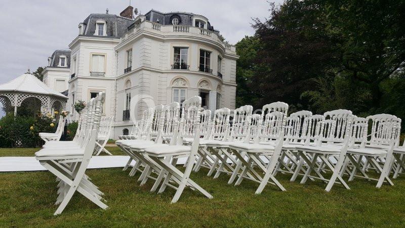 Chaises blanches alignées sur une pelouse devant un manoir, préparées pour un événement en extérieur.