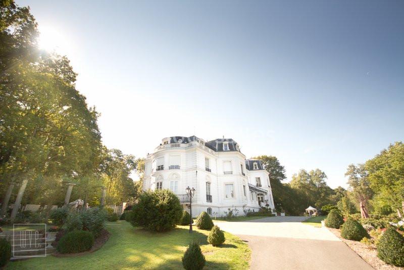 Façade d'un grand bâtiment blanc de style classique entouré de jardins verdoyants sous un ciel dégagé.