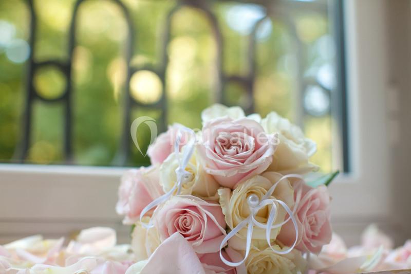 Bouquet de roses blanches et roses posé sur une surface près d'une fenêtre avec vue sur un jardin flou.