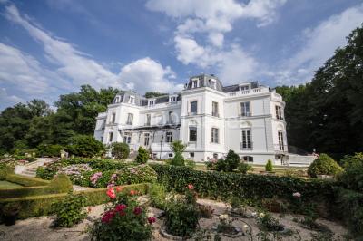 Allée bordée d'arbustes menant à une grande maison entourée d'arbres, capturée en noir et blanc.