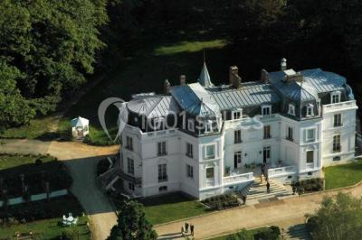 Allée bordée d'arbustes menant à une grande maison entourée d'arbres, capturée en noir et blanc.