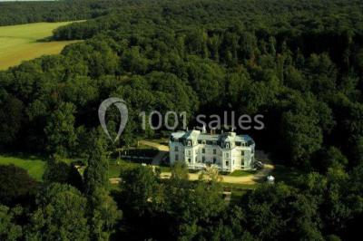 Allée bordée d'arbustes menant à une grande maison entourée d'arbres, capturée en noir et blanc.